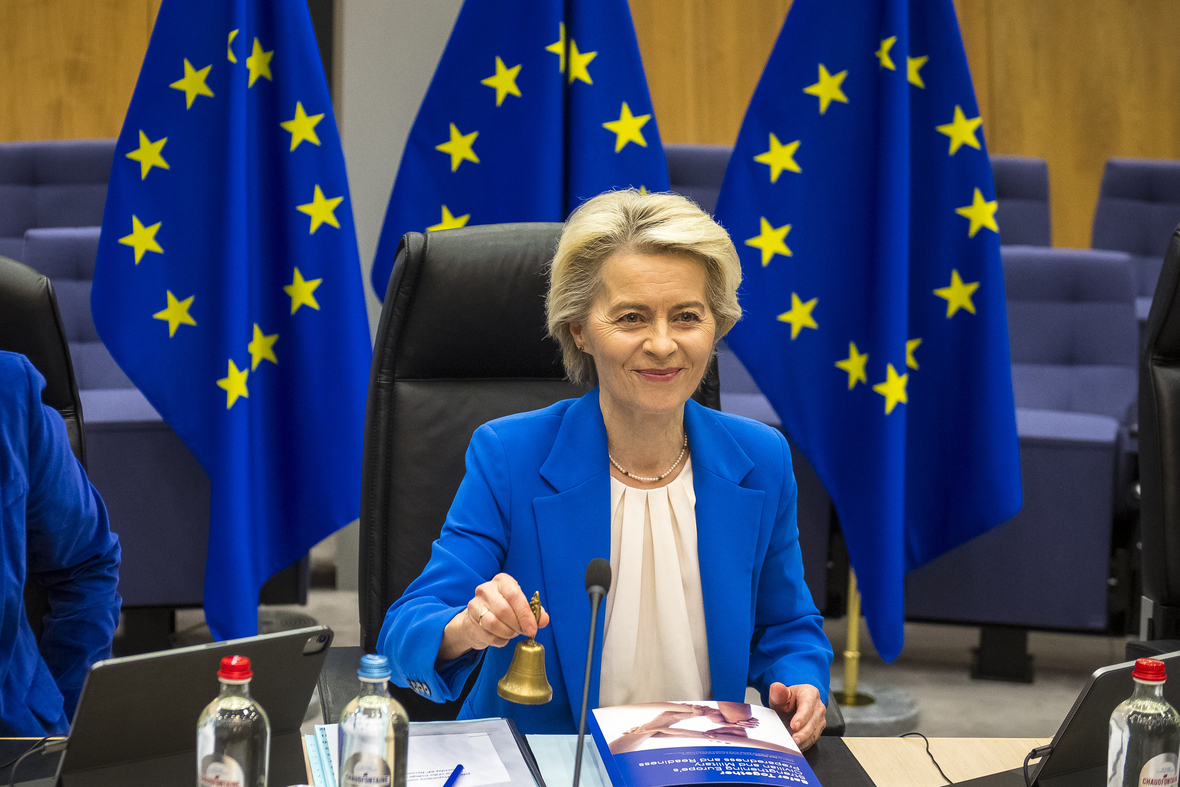 Ursula von der Leyen, Präsidentin der Europäischen Kommission, sitzt vor drei EU-Flaggen