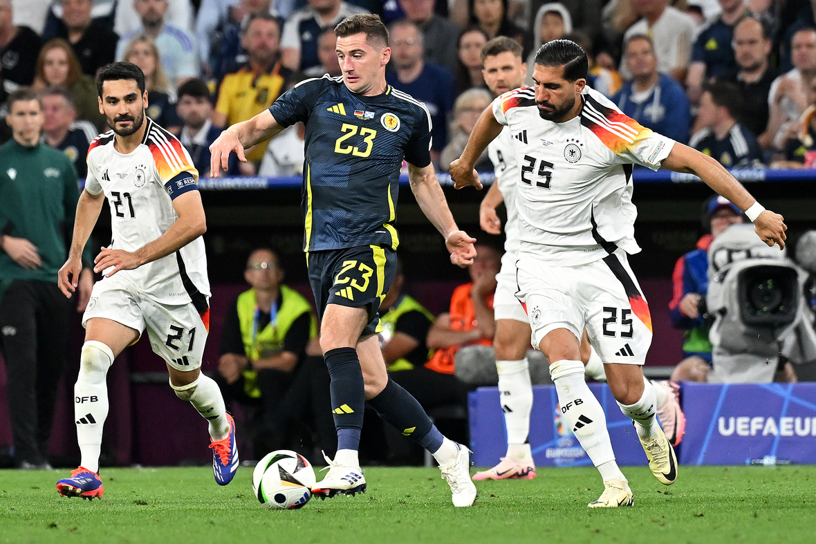 Spiel Deutschland gegen Schottland am 14.06.24 bei der UEFA EURO 2024. Das Bild zeigt den Zweikampf Kenny McLean (Schottland) und Emre Can (Deutschland). Im Hintergrund ist der Kapitän der Nationalmannschaft İlkay Gündoğan zu sehen.